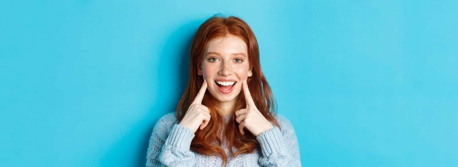 Smiling woman pointing to her teeth against a blue background
