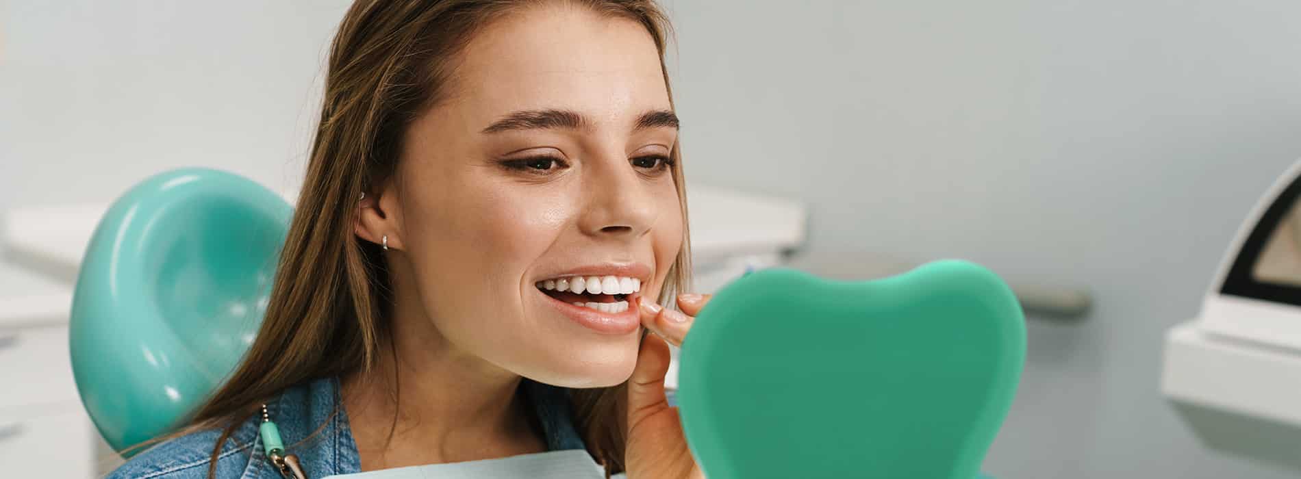 Woman in a dental chair using a hand mirror while pointing to her teeth during a dental visit
