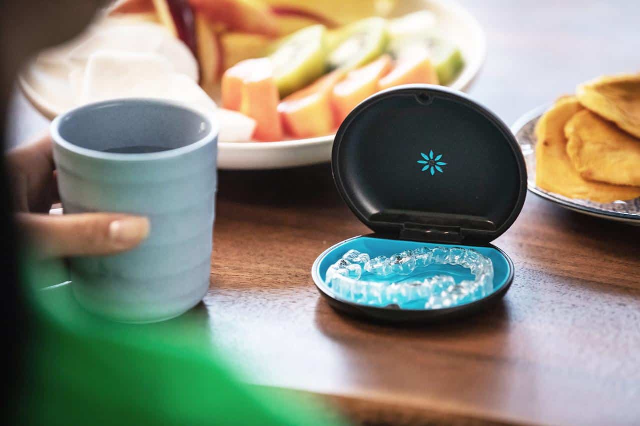 Clear Invisalign aligner stored in a travel case on a table beside a drink and meal while travelling.